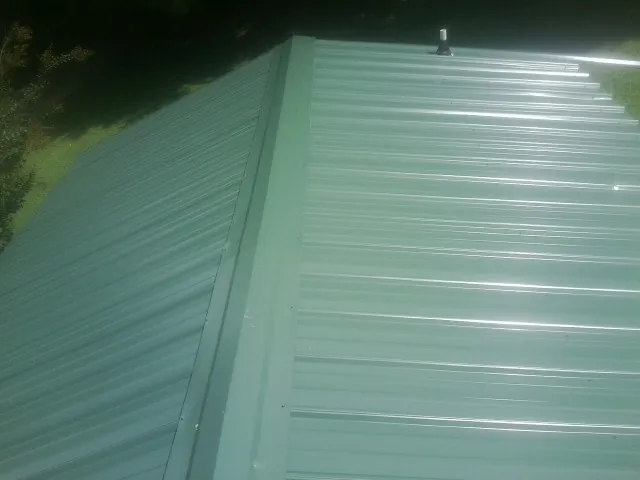 New green metal panels meeting at the ridge of a roof — Flat Roof Repair work by our crew in Savannah