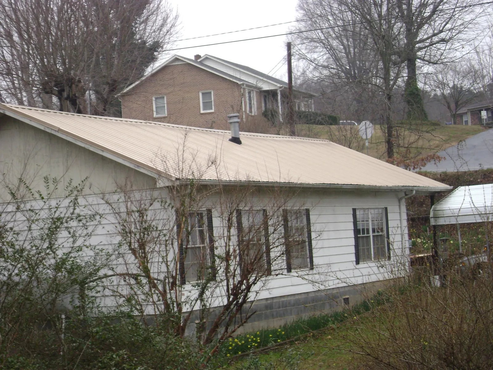 Tan metal roof on a white sided house set into a hillside — Commercial Roofing by Roofing Brothers in Savannah